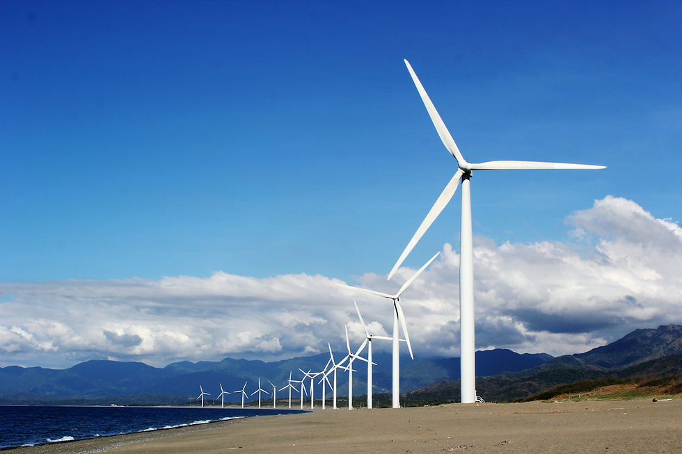 Row of wind turbines along a coastal landscape with mountains in the background, representing renewable energy production and sustainable practices.