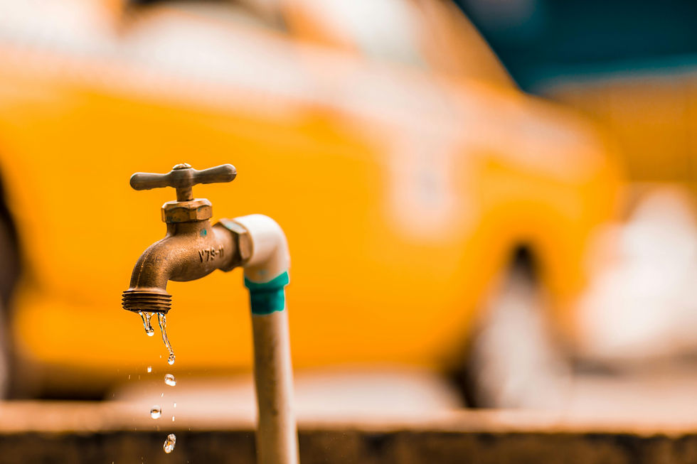 Close-up of a dripping faucet with blurred yellow taxi in background. Water droplets and orange tones create a vibrant urban scene.