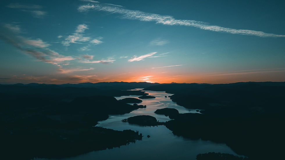 Aerial view of a serene lake with winding water channels at sunset. The sky is orange and blue with scattered clouds, creating a peaceful mood.