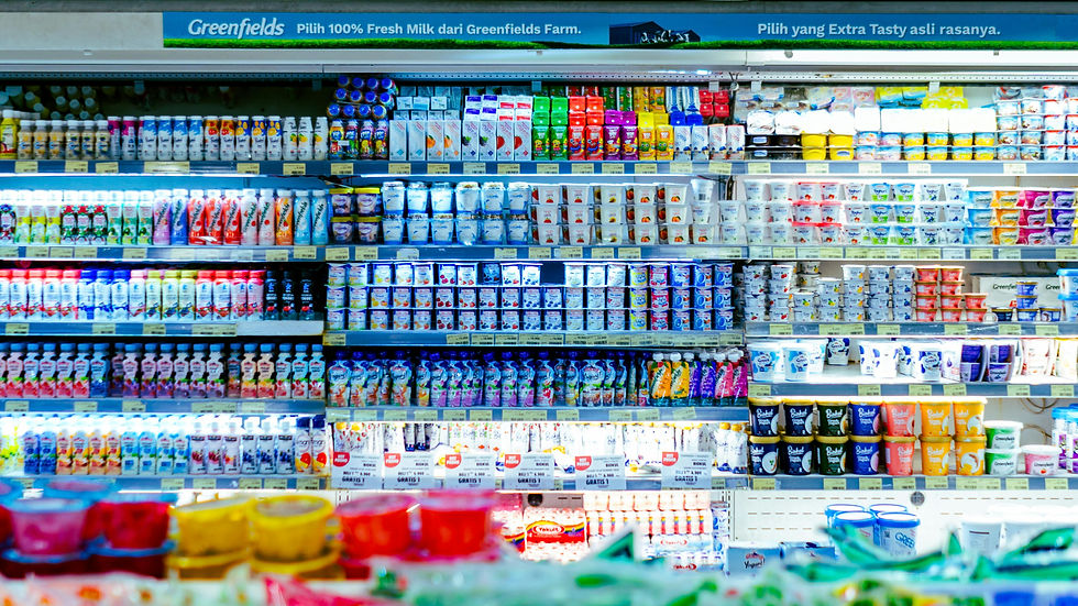 Dairy aisle stocked with various colorful yogurt and milk products. "Greenfields" sign above in a bright supermarket setting.