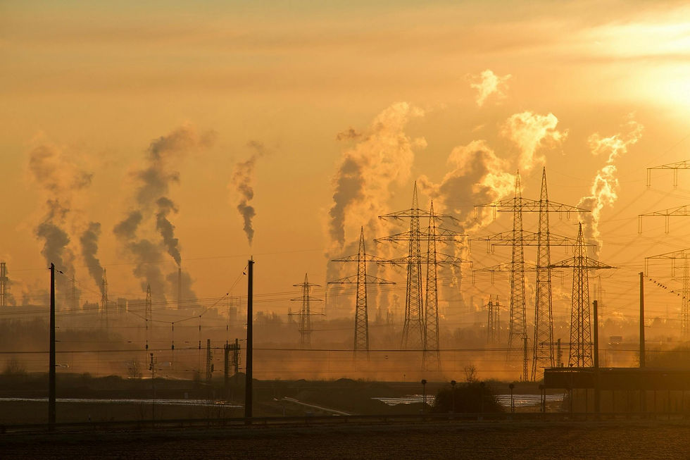 Industrial landscape with smokestacks emitting smoke against an orange sky. Power lines and a hazy atmosphere create a somber mood.